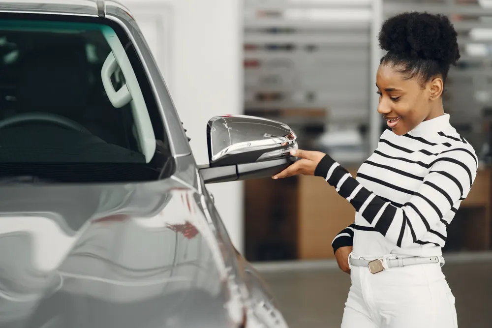 A woman looking over a silver car on a dealership floor