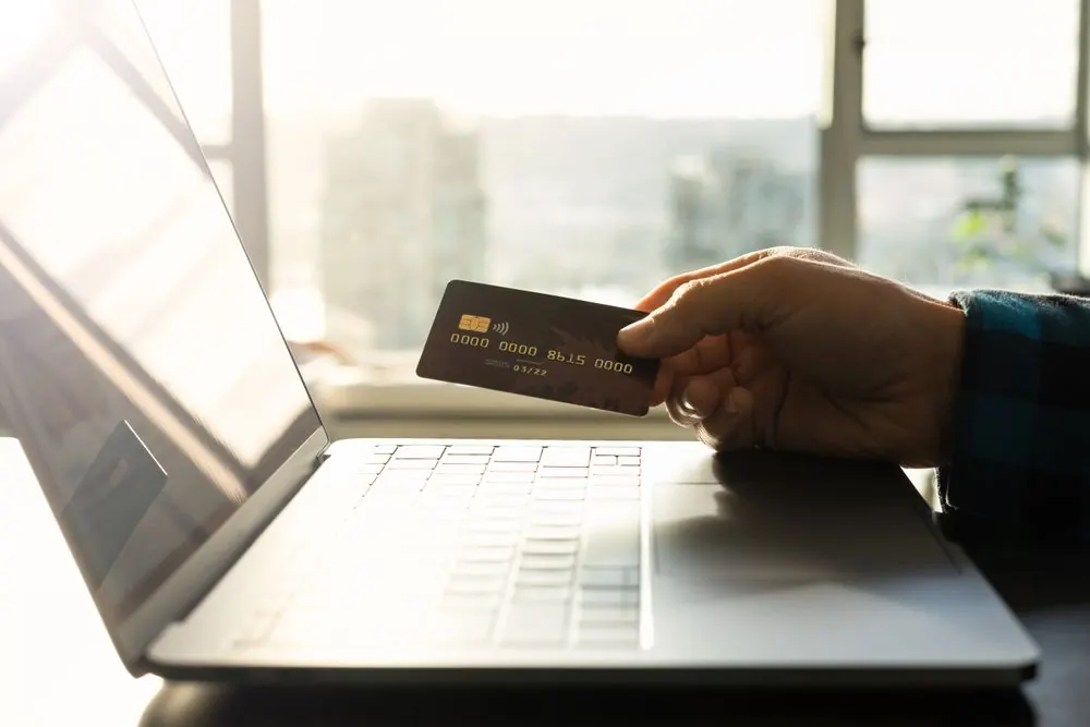 A bank card held beside an open laptop
