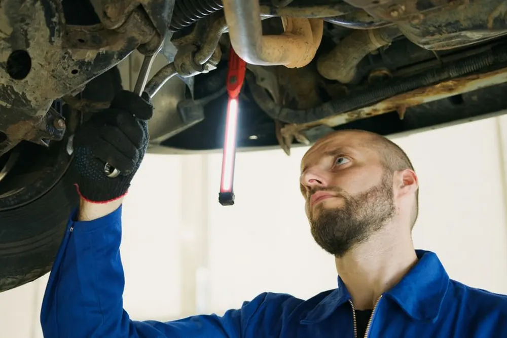 A technician under a car on a lift with an inspection lamp